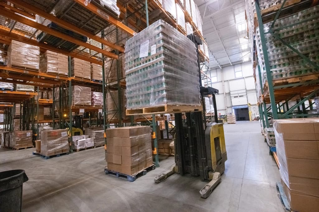 Wrapped pallets staged on warehouse racking with a forklift in the aisle